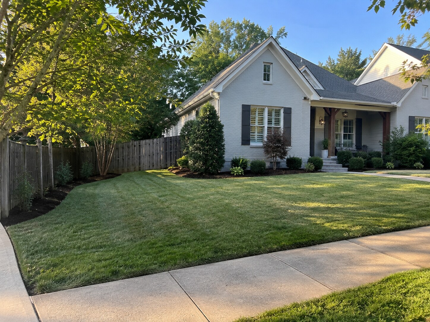 A white-brick cottage with its lawn freshly cut and the beds along the fence line cleared and edged.